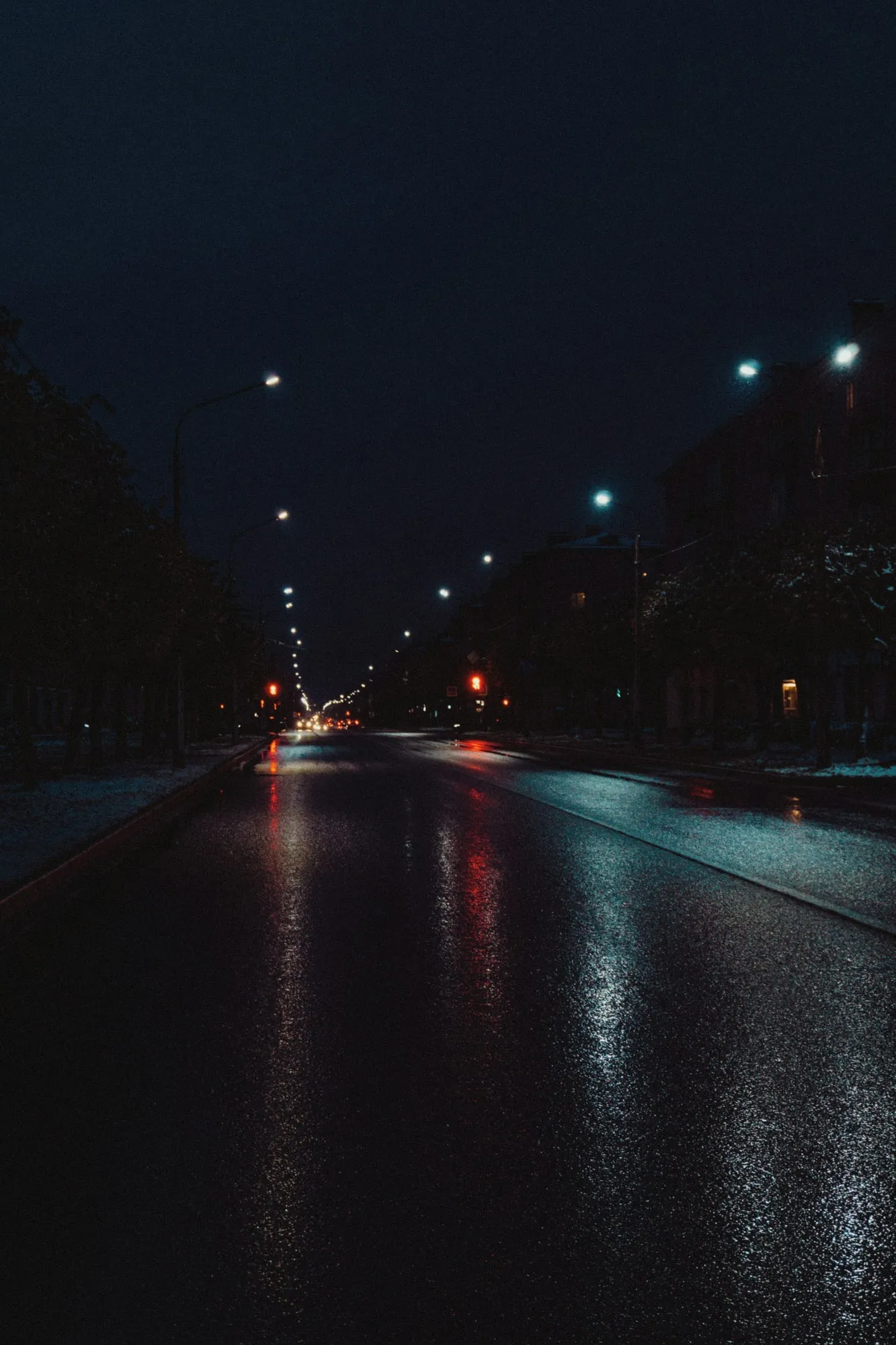 Stimmungsbild: nasse Fahrbahn bei Nacht, entgegenkommende Scheinwerfer spiegeln sich im Asphalt