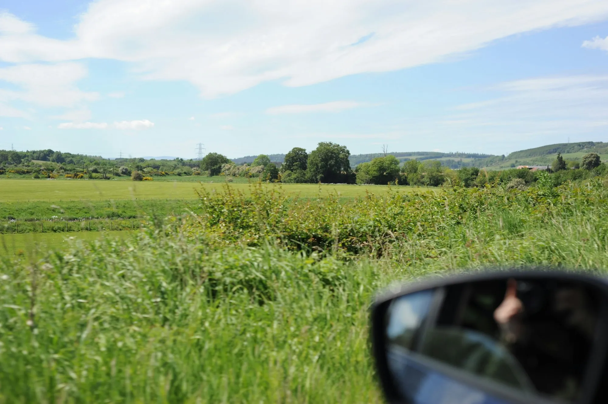 Stimmungsbild: Blick in den Seitenspiegel eines Autos auf Felder am Straßenrand