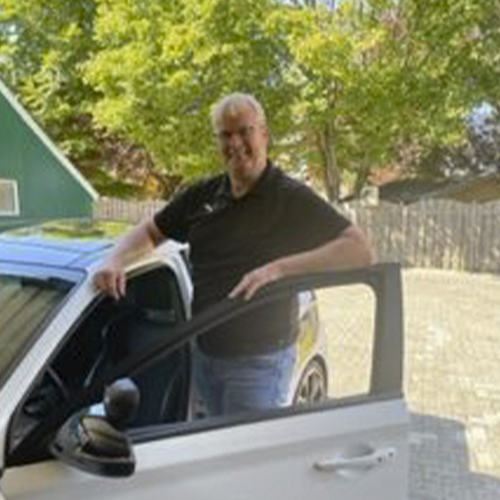 Hermann Behrens, Inhaber und Fahrlehrer, an der geöffneten Fahrertür eines Fahrschulwagens
